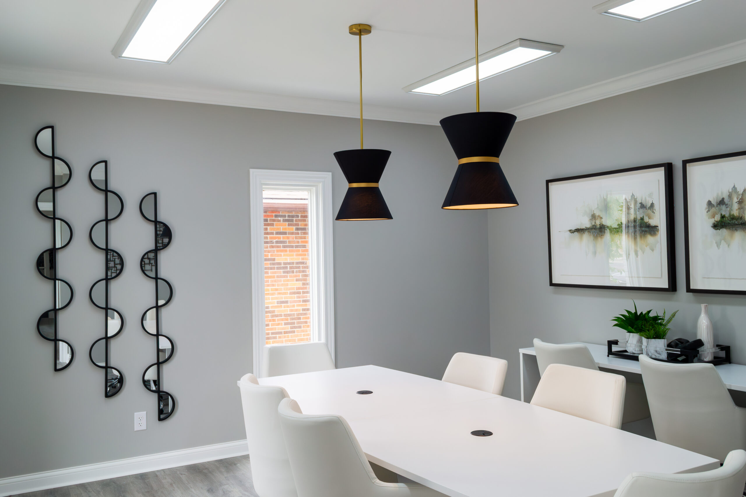 Image of a grey, office conference room with modern lights, mirrors, and artwork